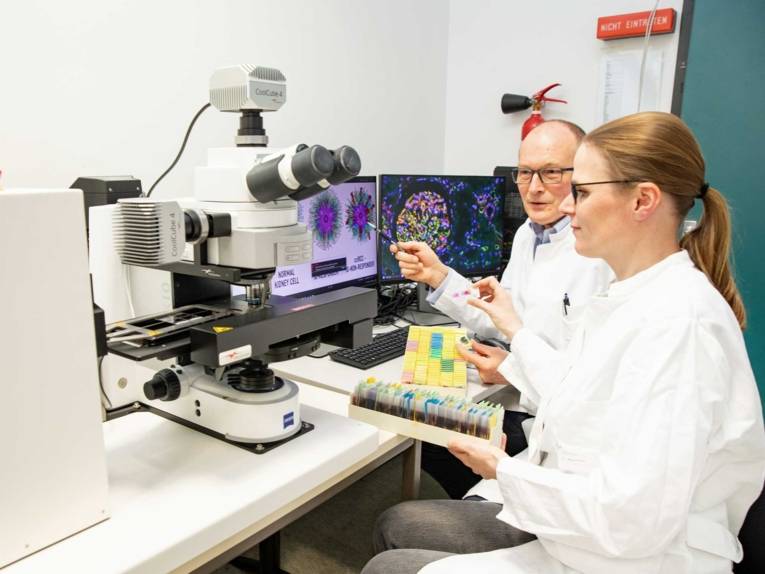 Eine Frau und ein Mann in weißen Kitteln sitzen vor einem Mikroskop