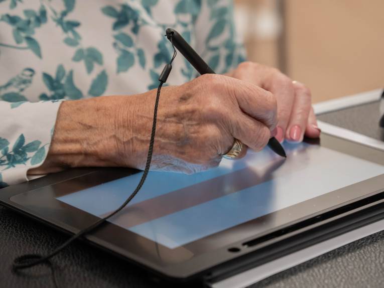 Eine Hand, die etwas auf einem Monitor unterschreibt.