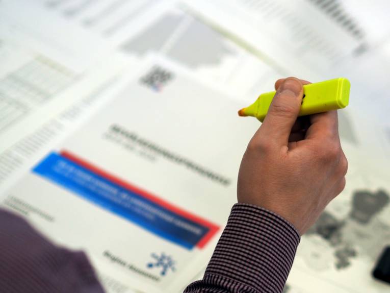 Jemand liest Unterlagen mit Regionslogo und markiert Text mit einem gelben Markerstift.