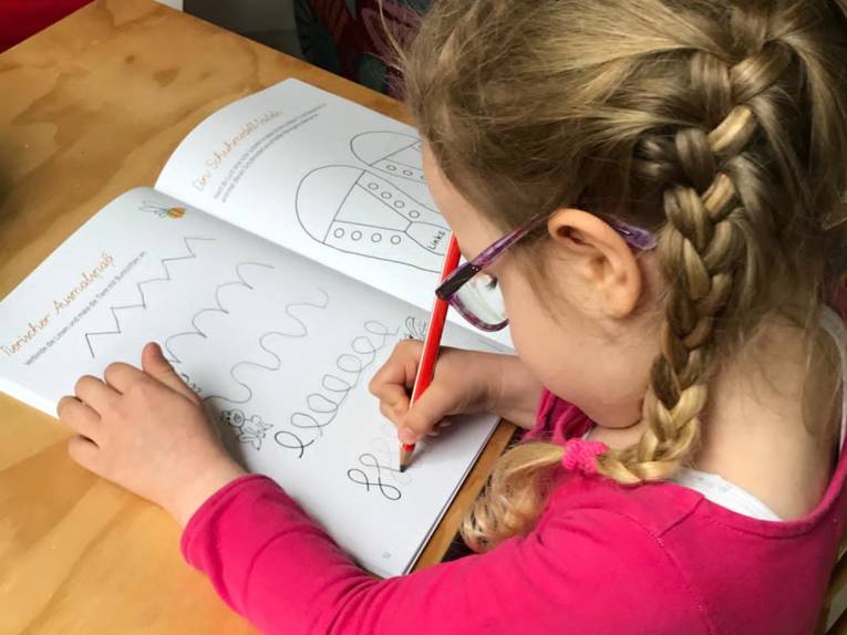 Ein Mädchen, an einem Kinderschreibtisch sitzend, malt in einem Ausmalbuch