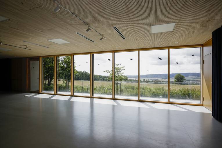 Multifunktionsraum mit großer Fensterfront und Blick in die Natur