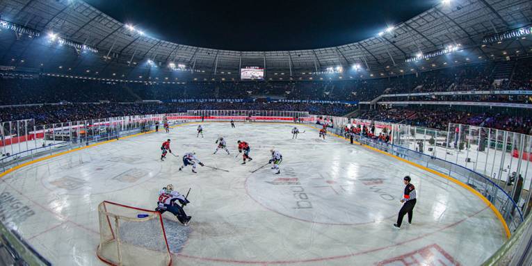 Blick in ein Fußballstadion mit einem Eishockeyfeld, auf dem ein Spiel stattfindet.