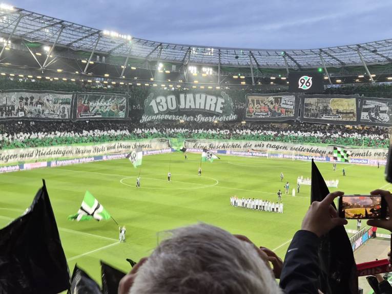 Blick von der Südkurve auf Plakate, Fahnen und riesige Tansparente im vollbesetzten Fußballstadion von Hannover 96.