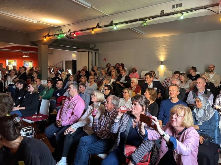 Viele Menschen sitzen auf Stühlen und hören sich die Rede an