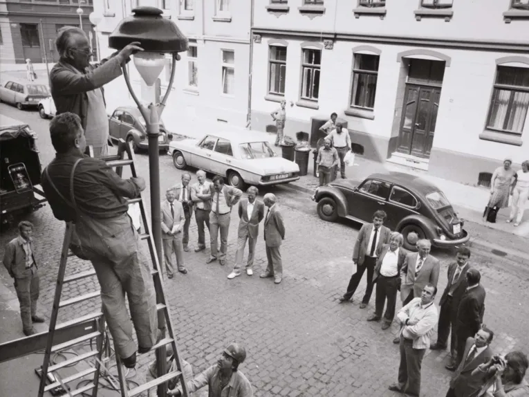 Arbeiter auf einer Leiter an einer Straßenlaternen. Historische Schwarz-Weiß-Aufnahme