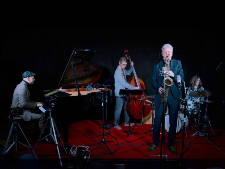 Auf dem Bild sind drei Männer und eine Frau zu sehen, die an ihre Instrumenten spielen.