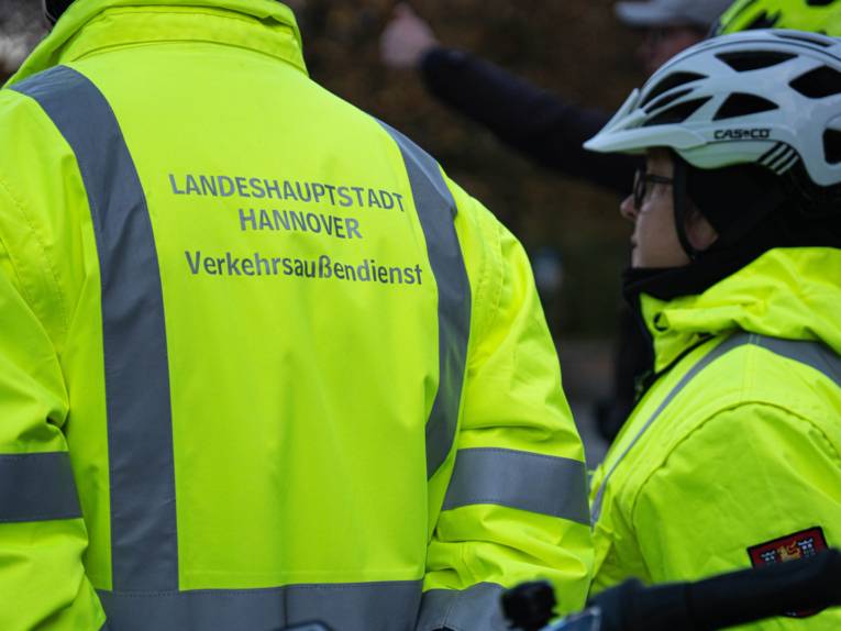 Zwei Personen mit gelben Jacken. Darauf steht "Landeshauptstadt Hannover Verkehrsaußendienst ".