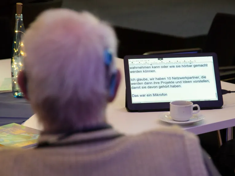 Ein Herr mit Cochlear-Implantat liest den Text auf einem Tablett vor ihm