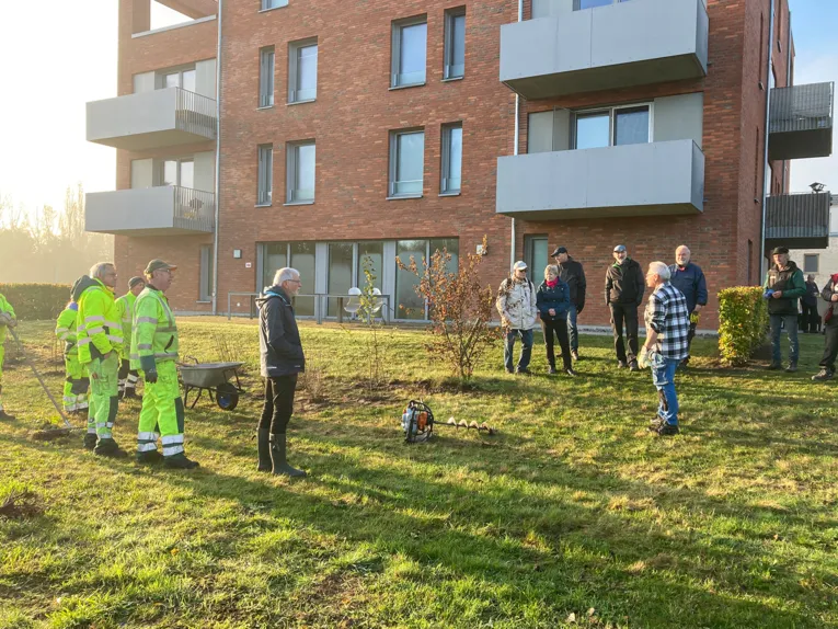 Menschen auf einer Gr&uuml;nfl&auml;che vor einem Haus.