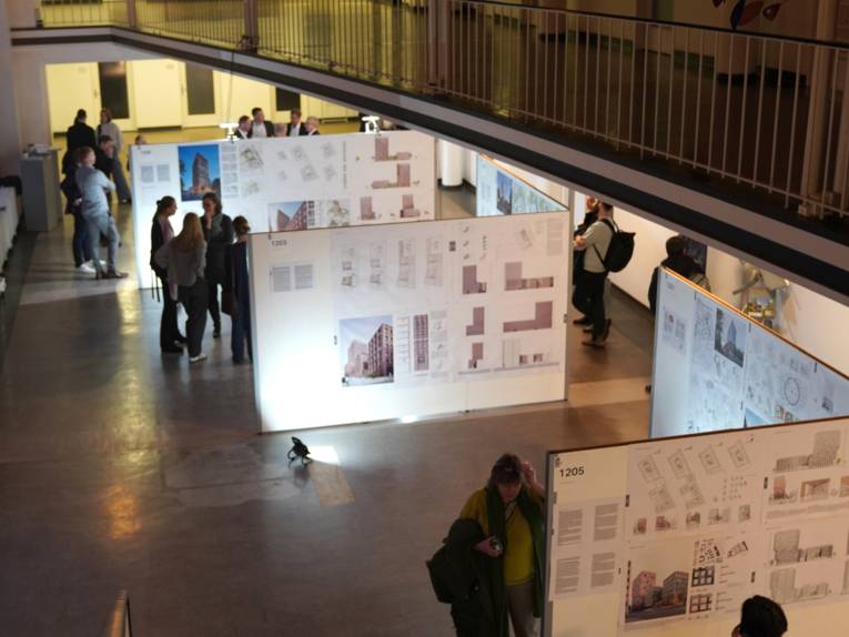 Menschen stehen zwischen Aufstellwänden, an denen Bilder, Text und Zeichnungen angebracht sind.