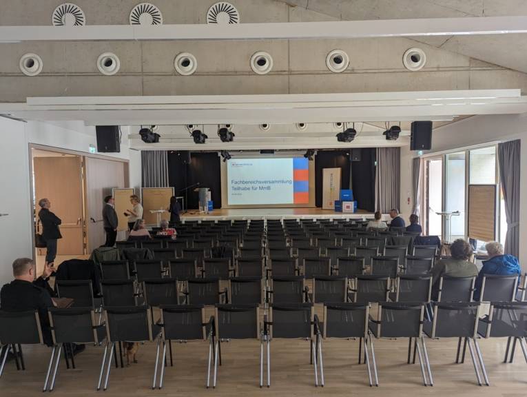 Der Saal des Stadtteilzentrums mit Blick auf die Bühne mit Leinwand. Im Zuschauerraum: Reihenbestuhlung.
