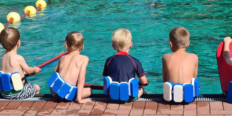 Drei Kinder mit Schwimmhilfen am Beckenrand im Freibad