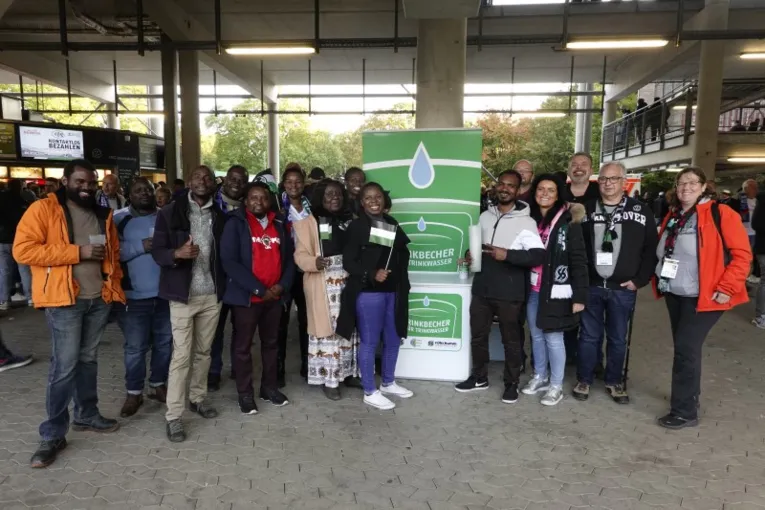 Eine Gruppe Personen mit Trinkbechern und Hannover 96-Fahnen an einem Infostand im Fu&szlig;ballstadion