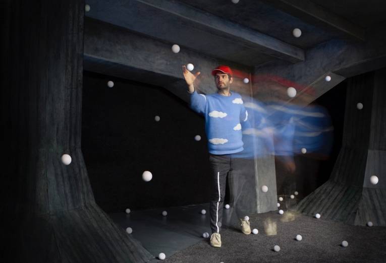 Ein Mann spielt mit Jonglierbällen in einem dunklen Raum. Viele Bälle fliegen schwerelos durch den Raum.