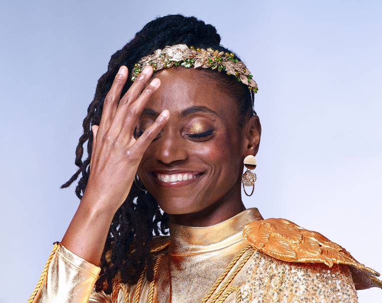 Lachende Frau mit geschlossenen Augen, langen Rastazöpfen, Perlenstirnband und goldverziertem Oberteil