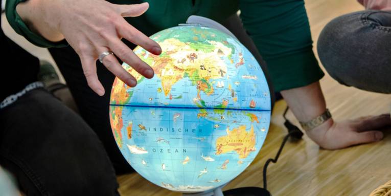 Person zeigt mit den Fingern einer Hand etwas auf einem beleuchteten Globus.