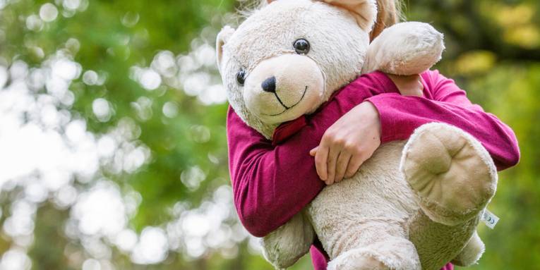 Ein Kind hält einen großen Teddybären vor der Brust.