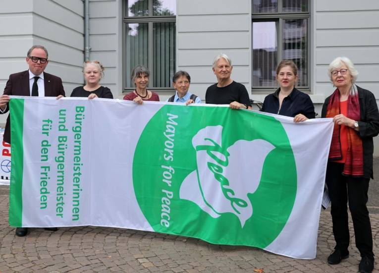 Bürgermeister Timo Kühn hat die Fahne mit der Aufschrift „Bürgermeister für den Frieden“ vor dem Krefelder Rathaus zusammen mit Friedensaktivisten gehisst.