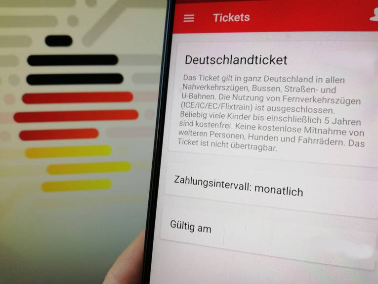 Foto eines Bildschirms und eines Handydisplays, auf dem das Deutschlandticket gekauft wird
