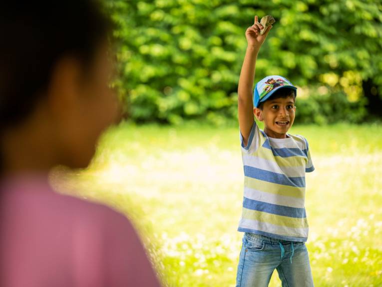 Ein Junge steht im Grünen und meldet sich wie in der Schule