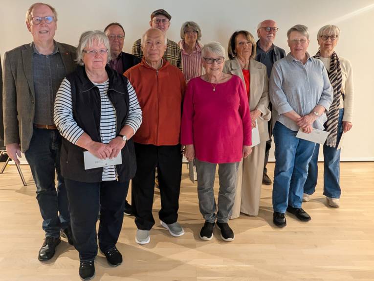 Eine Gruppe von über 60-jährigen Frauen und Männern auf einem Gruppenbild in einem Raum einem weißen Hintergrund.