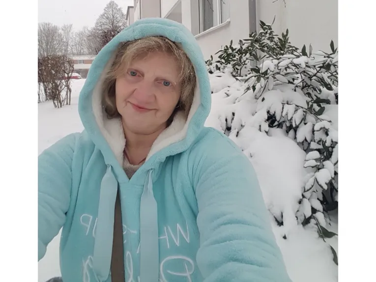 Eine Frau in einem dicken Fleecepulli mit Kapuze in winterlicher Umgebung.