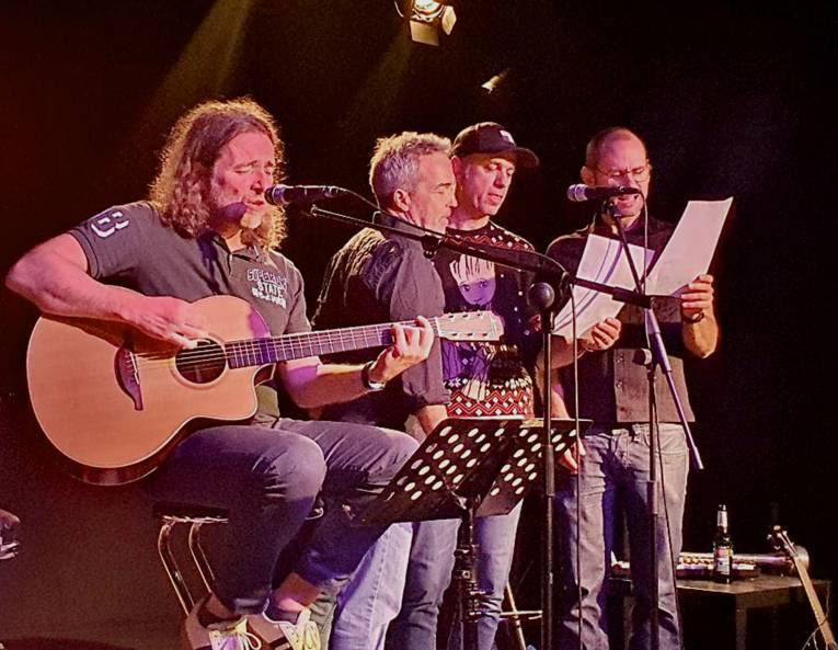 Vier Männer auf einer Bühne, einer mit Gitarre