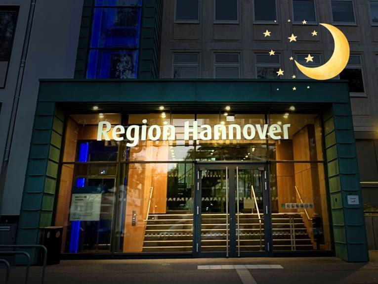 Ein Gebäude mit einem großen Eingang aus Glas der beleuchtet ist, der übrige Teil des Bilds ist dunkel. Über dem Eingang steht "Region Hannover".