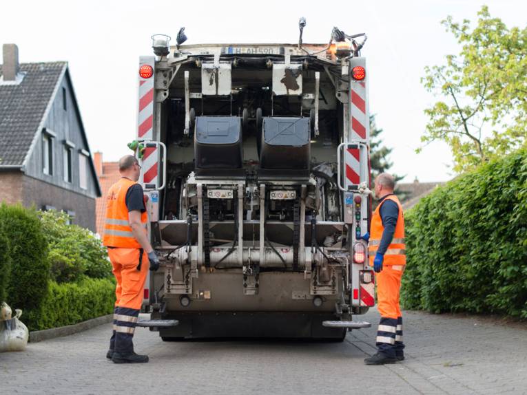 Zwei Männer in signalfarbener Arbeitskleidung an einem Müllfahrzeug.