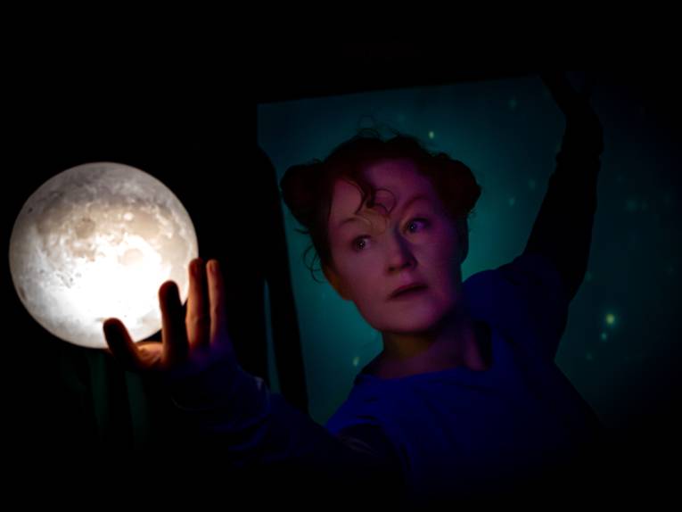 Theaterszene: Eine Frau schaut auf ihre Hand und den Mond in ihrer Hand.