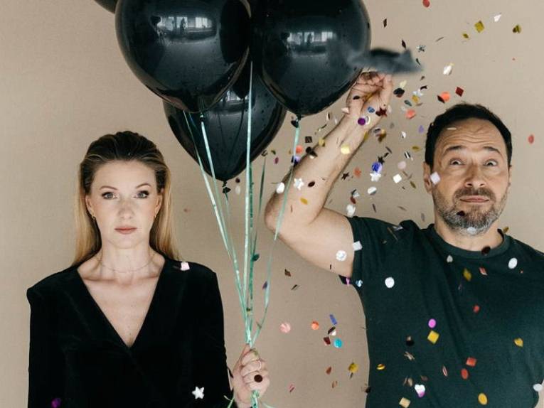 Eine Frau mit langem Haar und drei Luftballons und ein Mann, der Konfetti über seinem Kopf ausstreut.