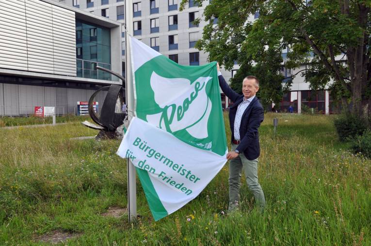 Landrat Thomas Will vom Landkreis Groß-Gerau breitet die Mayors for Peace Flagge aus