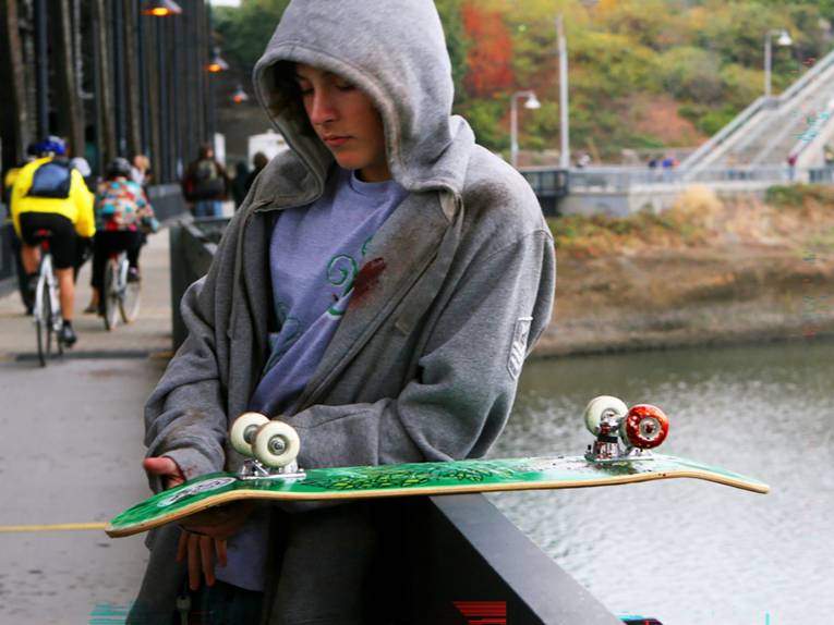 ein Mann lehnt an einer Mauer, auf der ein Skateboard liegt.