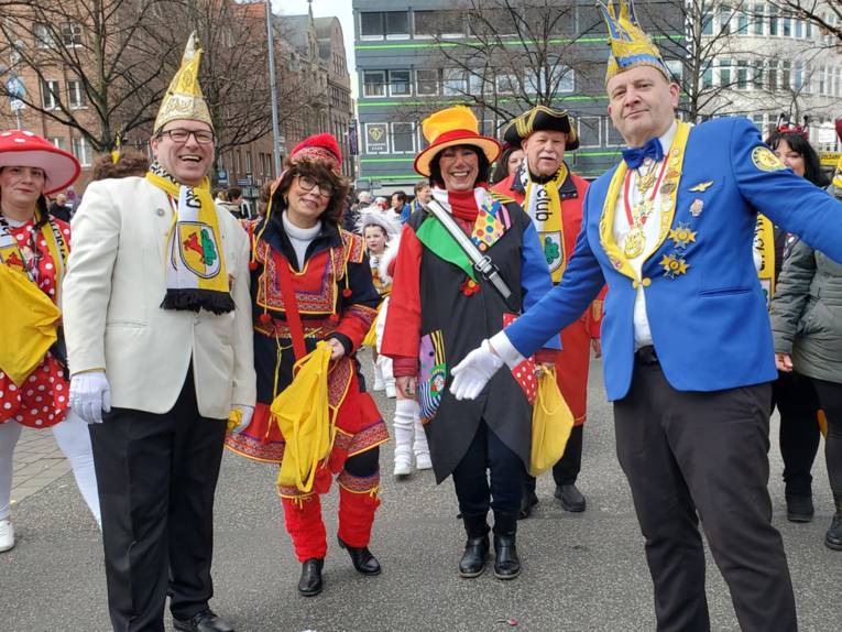 Im Vordergrund stehen zwei Männer in Karnevalsuniformen, dahinter eine Personengruppen in Karnevalskostümen.