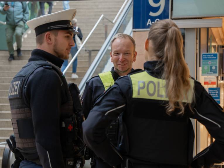 Drei Personen reden miteinander. Zwei von ihnen tragen eine Polizeiuniform, eine trägt die Kleidung des Ordnungsdienstes der LHH.