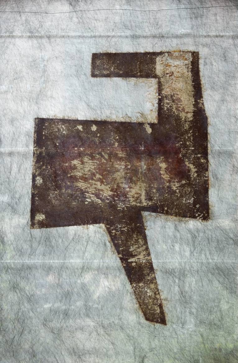 Zu sehen ist eine grafische Arbeit von Hartmut Stielow. Hier ist mithilfe eines chemischen Prozesses ein Druck aus Rost auf ein Vlies übertragen worden. Der Druck zeigt eine hartkantige, geometrische Figur.