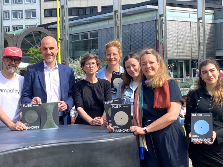 Gruppenfoto am Outdoor-Piano auf dem Opernplatz. Von links nach rechts: Rapper Spax, Oberbürgermeister Belit Onay, Friederike Ankele (Leiterin des städtischen Kulturbüros), Inga Samii (Fachbereichsleitung Kultur), Sina Hensel (Geschäftsführerin Musikland Niedersachsen), Bildungs- und Kulturdezernentin Eva Bender sowie die Sängerin und Songwriterin Amapola.