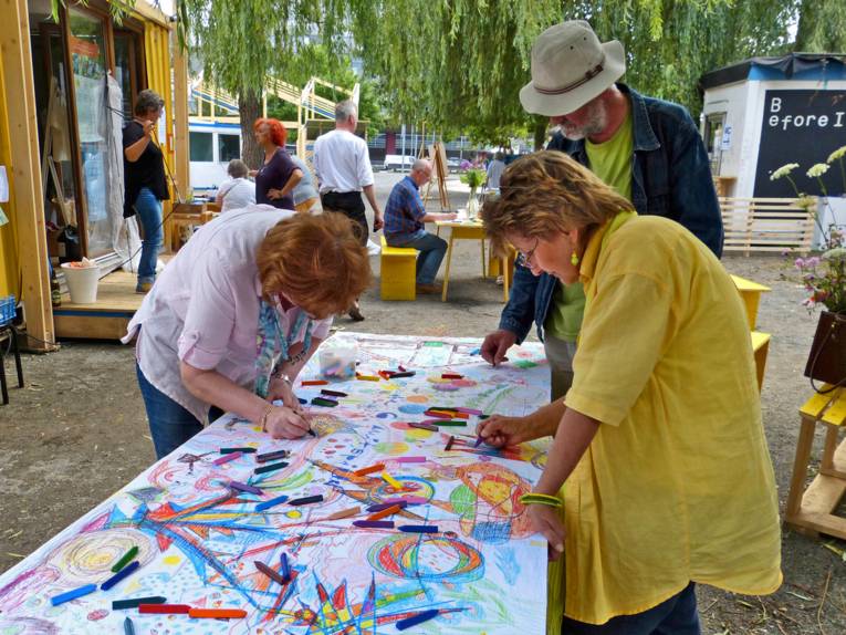 Drei Teilnehmer malen auf einem großen Stück Papier mit bunter Farbe