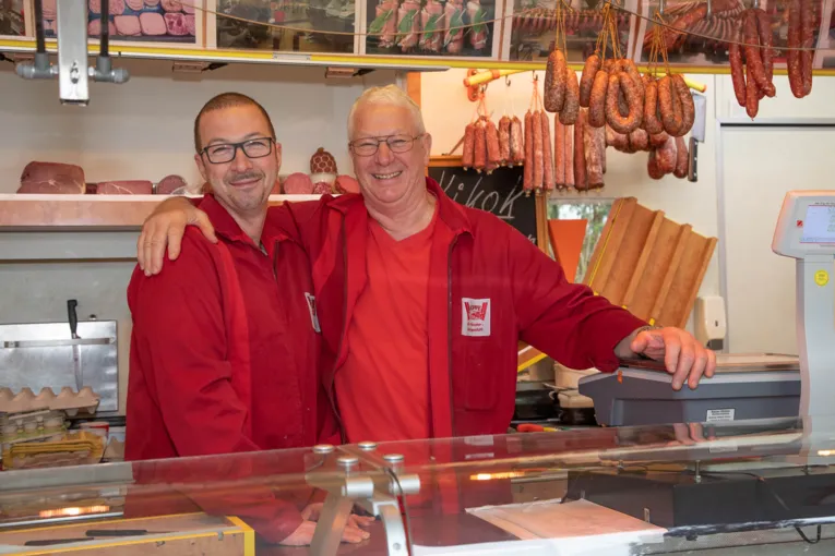 Zwei M&auml;nner l&auml;cheln in die Kamera. Einer hat einen Arm &uuml;ber die Schulter des anderen gelegt.