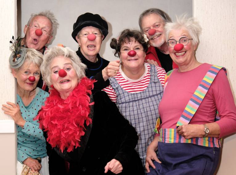 Fünf Frauen und zwei Männer mit Clownsnasen und bunter Kleidung.