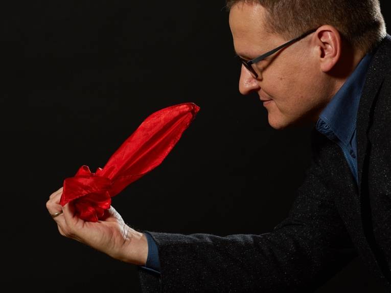 Mann mit kurzem Haar und Brille hält ein gefaltetes Tuch in der Hand.