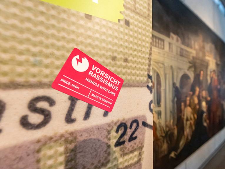 Blick in die Sonderausstellung "Von goldenen Kutschen und kolonialer Vergangenheit: Hannover, England und die Sklaverei", vom 12. Juli bis 13. November 2022 im HMH, hier der rechteckige rote Sticker "Vorsicht Rassismus"