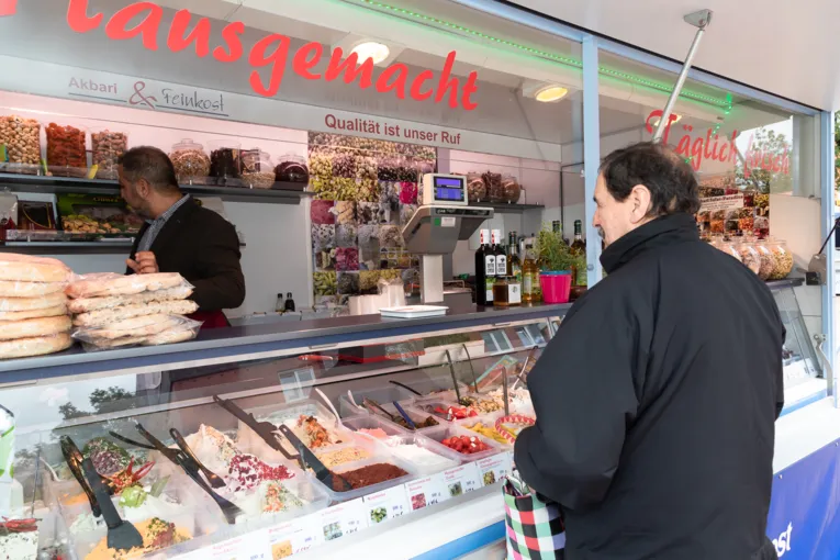 Verk&auml;ufer und Kunde an einem Marktwagen, wo Feinkost verkauft wird.