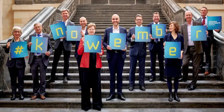 Menschen stehen auf einer großen Treppe und halten Tafeln in den Händen, die den Begriff #knowember bilden.
