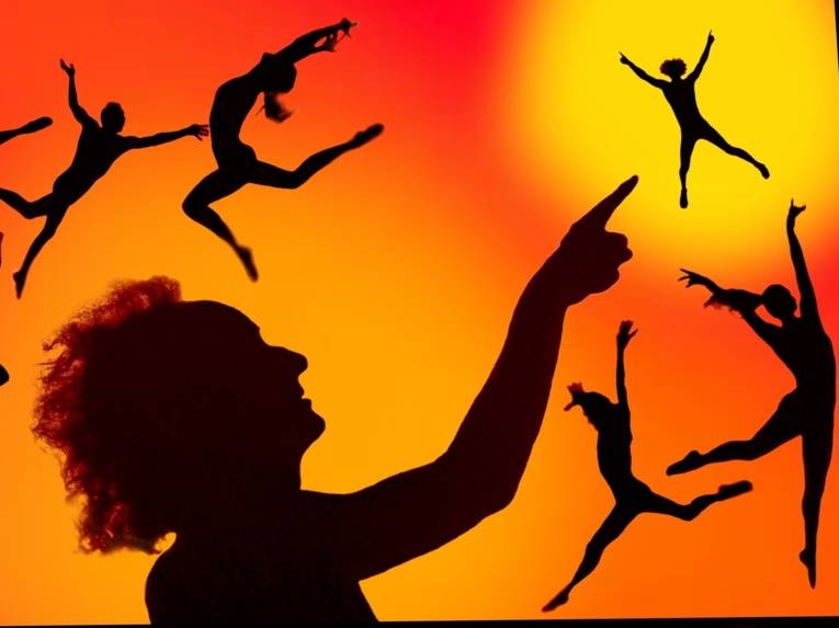 Zu sehen sind Menschen-Silhouetten in athletischen Bewegungen vor einem rot-orange-gelben Hintergrund.