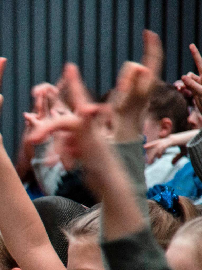 Kinder heben ihre Arme und Finger und signalisieren dadurch, dass sie etwas beitragen oder eine Frage stellen wollen.