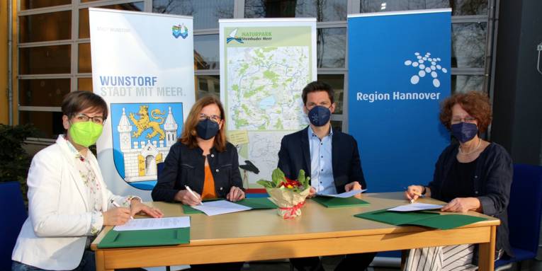 Drei Frauen und ein Mann sitzen an einem Tisch und unterschreiben Dokumente.