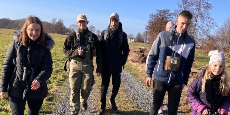Sechs Personen gehen auf einem Feldweg.