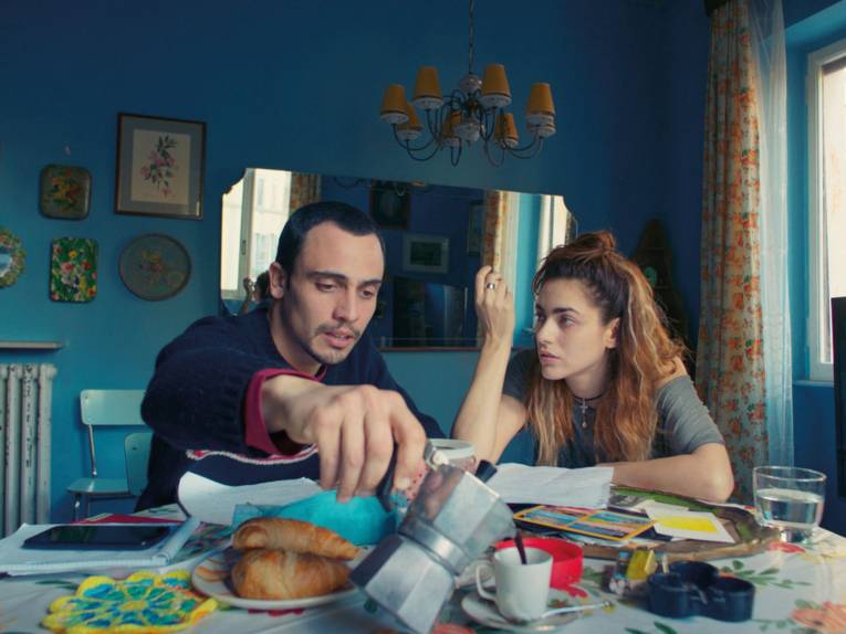 Das Foto zeigt Renato (links) und Anna (rechts) die zusammen am tisch sitzen, sie führen eine Diskussion und frühstücken währenddessen.