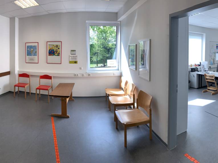 Blick in zwei Räume, einen Warteraum und ein Büroraum mit Schreibtisch, Stuhl und Rechner